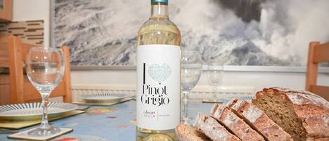 A table with a bottle of Pinot Grigio wine, a loaf of bread, and a painting of a seascape in the background.