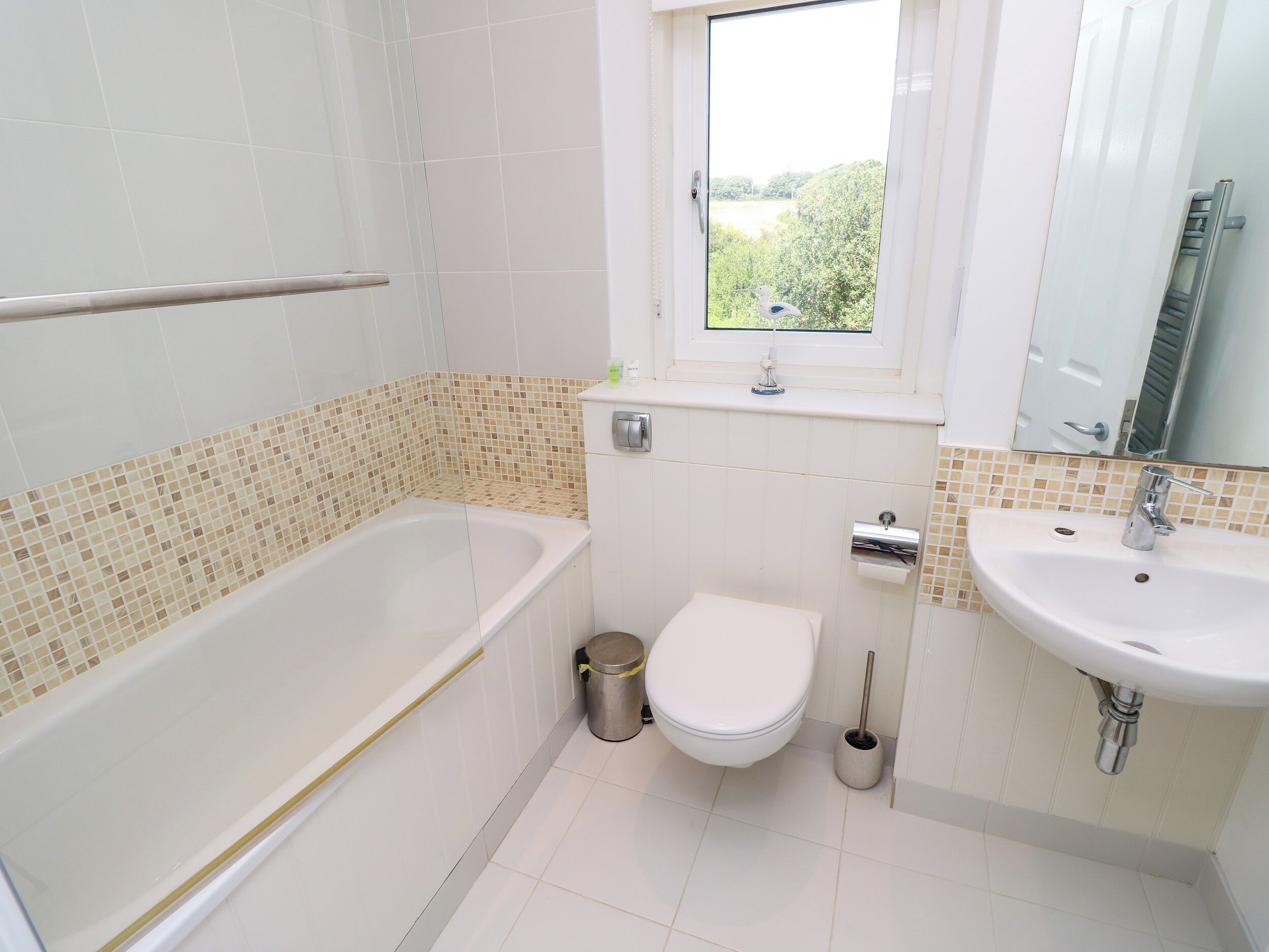 Une salle de bain équipée d’une baignoire, de toilettes, d’un lavabo et d  ’une fenêtre donnant sur un espace verdoyant.