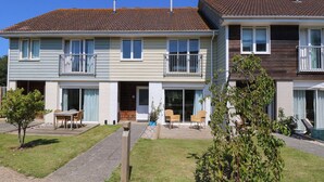 A two-story residential building with a tiled roof, a small front yard with a wooden table and chairs, and a potted plant. - Whitfield P10 (Yarmouth)