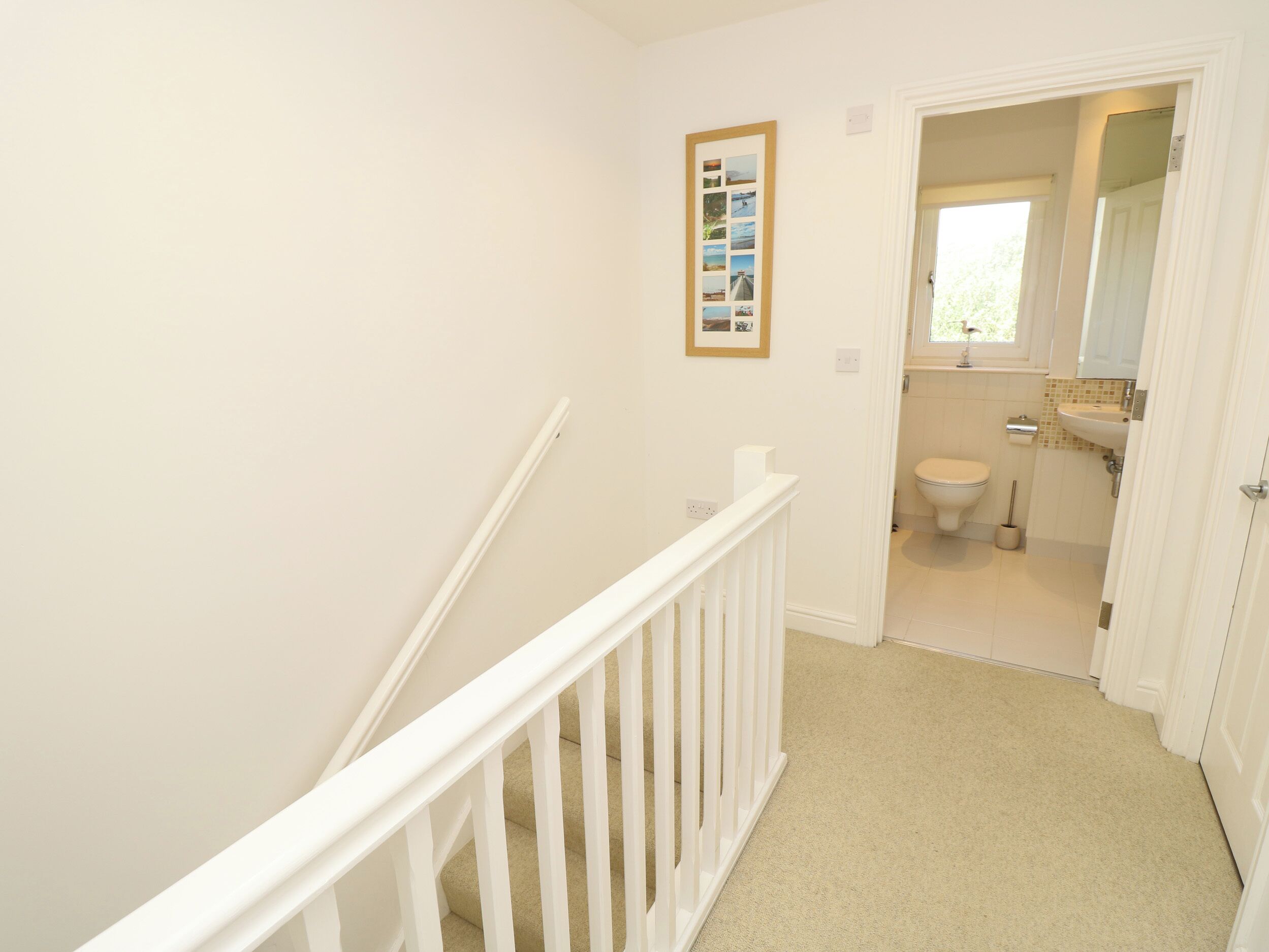 A narrow hallway leading to a bathroom with a toilet, sink, and a framed photo collage on the wall.