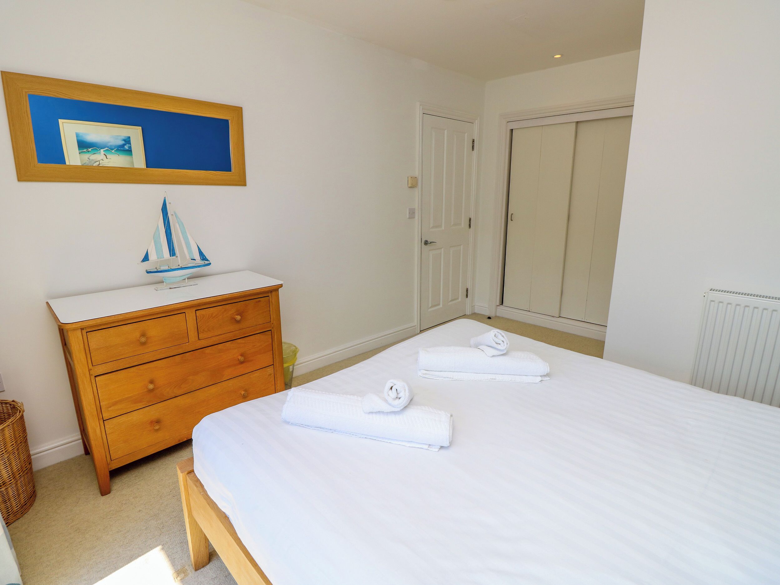 A bedroom with a bed, a wooden dresser, a framed picture, and a closet.