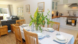 A dining area with a table set for four, surrounded by wooden chairs, a vase with flowers, and a view of the kitchen in the background. - Whitfield P10 (Yarmouth)