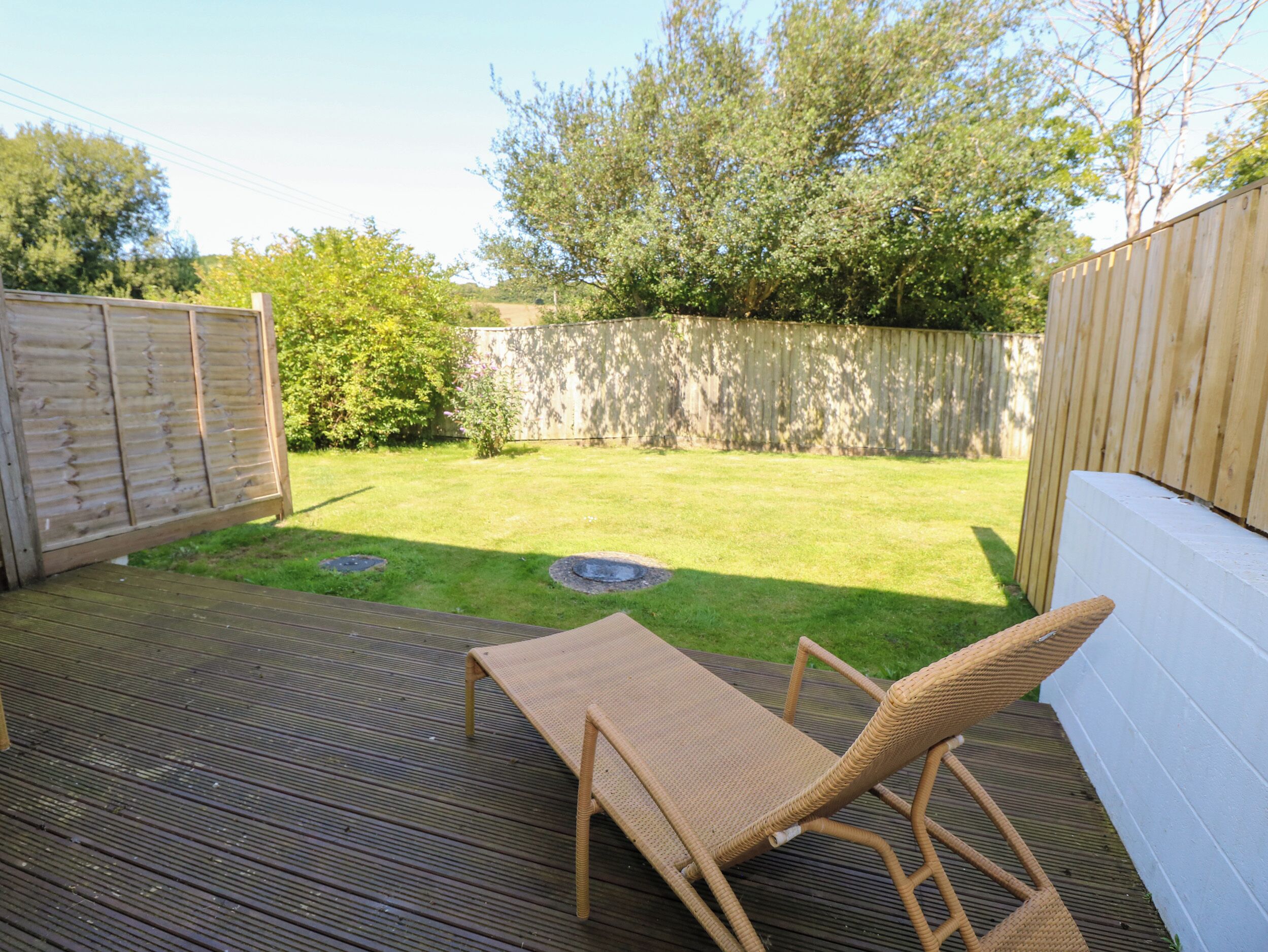 Una terraza de madera con una silla y una mesa de mimbre, rodeada por una valla de madera y un césped.