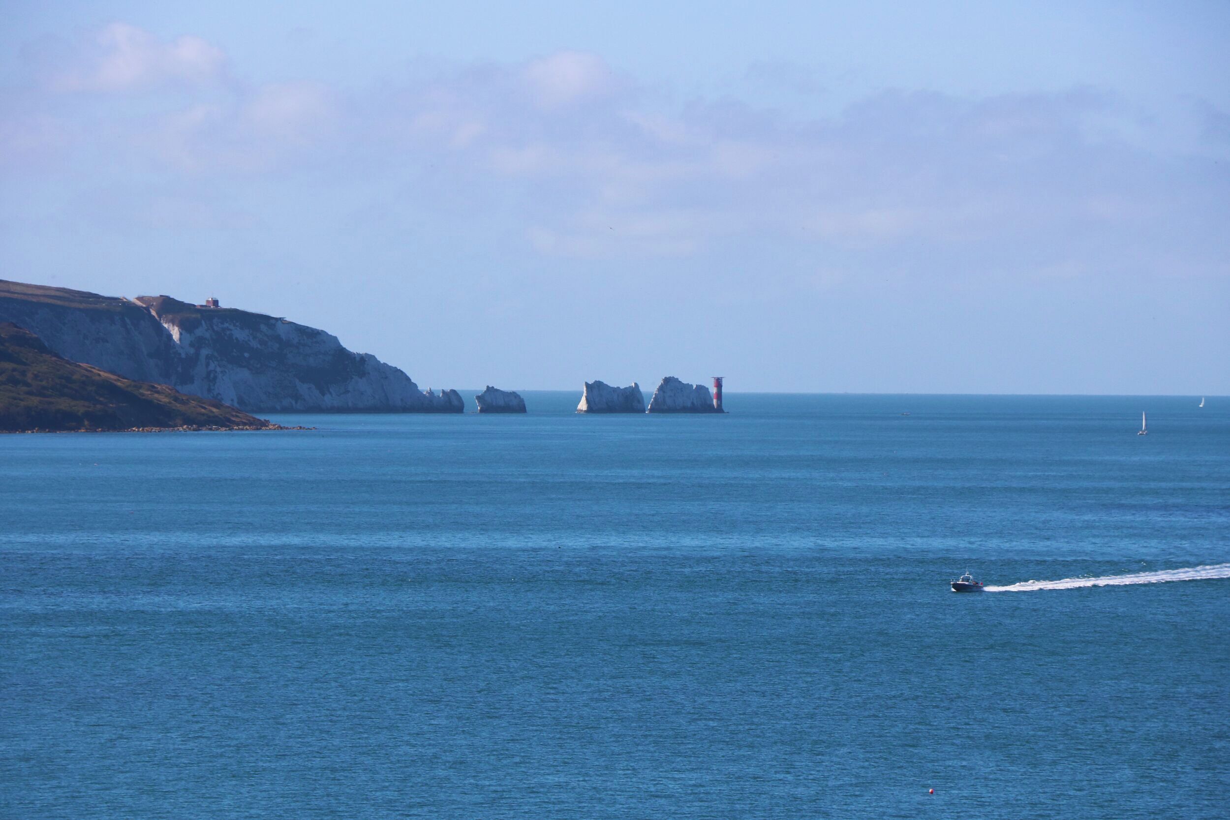A coastal scene with cliffs, a lighthouse, and a boat on the water.