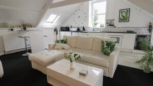 A modern loft apartment with a high ceiling, a kitchenette, a living area with a sofa and coffee table, and a dining area. - The Old Workshop (Llanybydder)