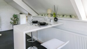 A modern dining area with a white table set for two, a black vase with greenery, and a white radiator below. - The Old Workshop (Llanybydder)
