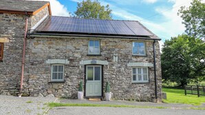 A stone building with a grey door, two windows, and a solar panel roof. - The Old Workshop (Llanybydder)