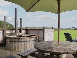 Une terrasse extérieure en bois, dotée d’un jacuzzi, d’une table et d’un banc.