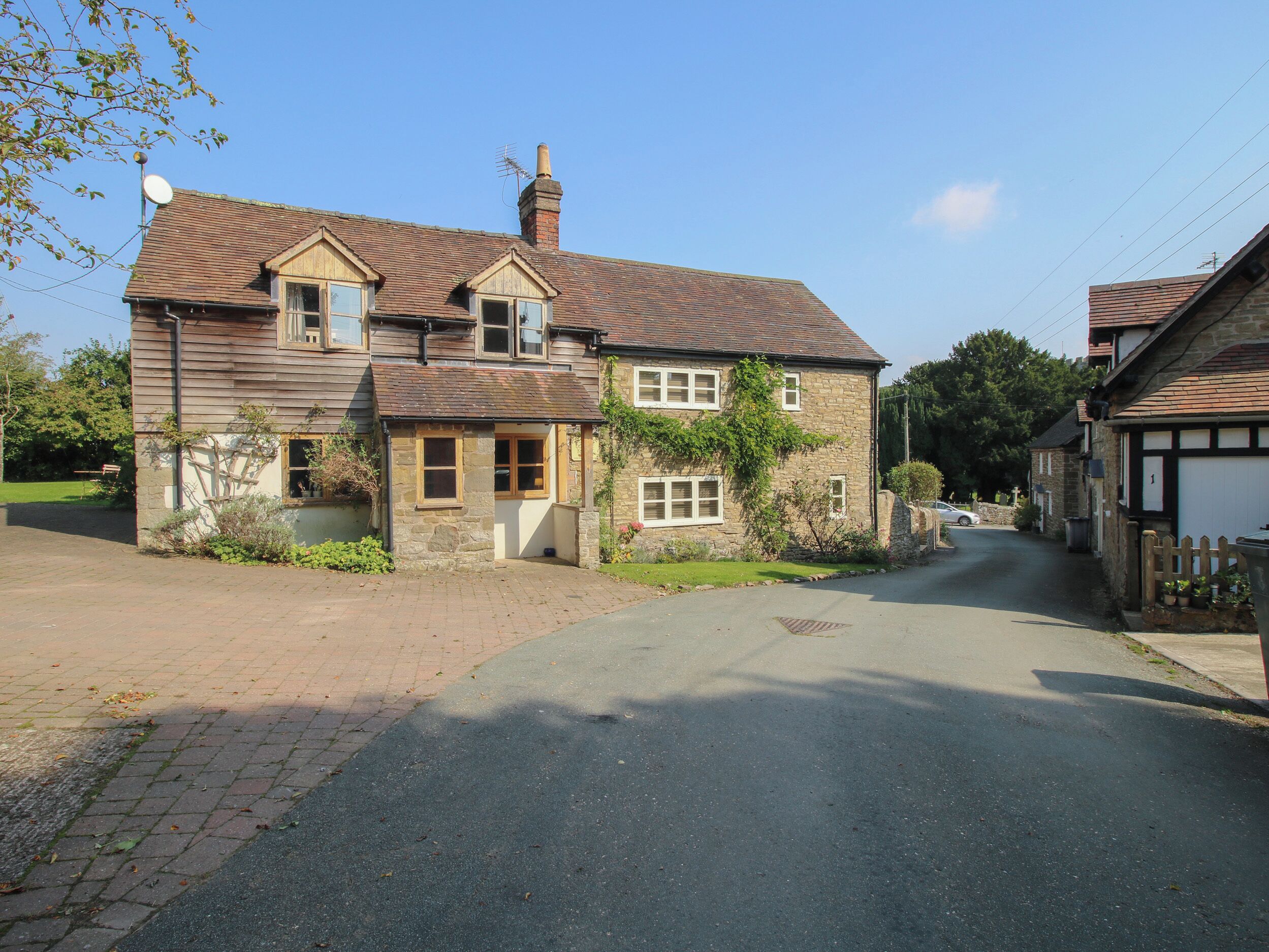 A two-story stone house with a tiled roof, a chimney, and a satellite dish.