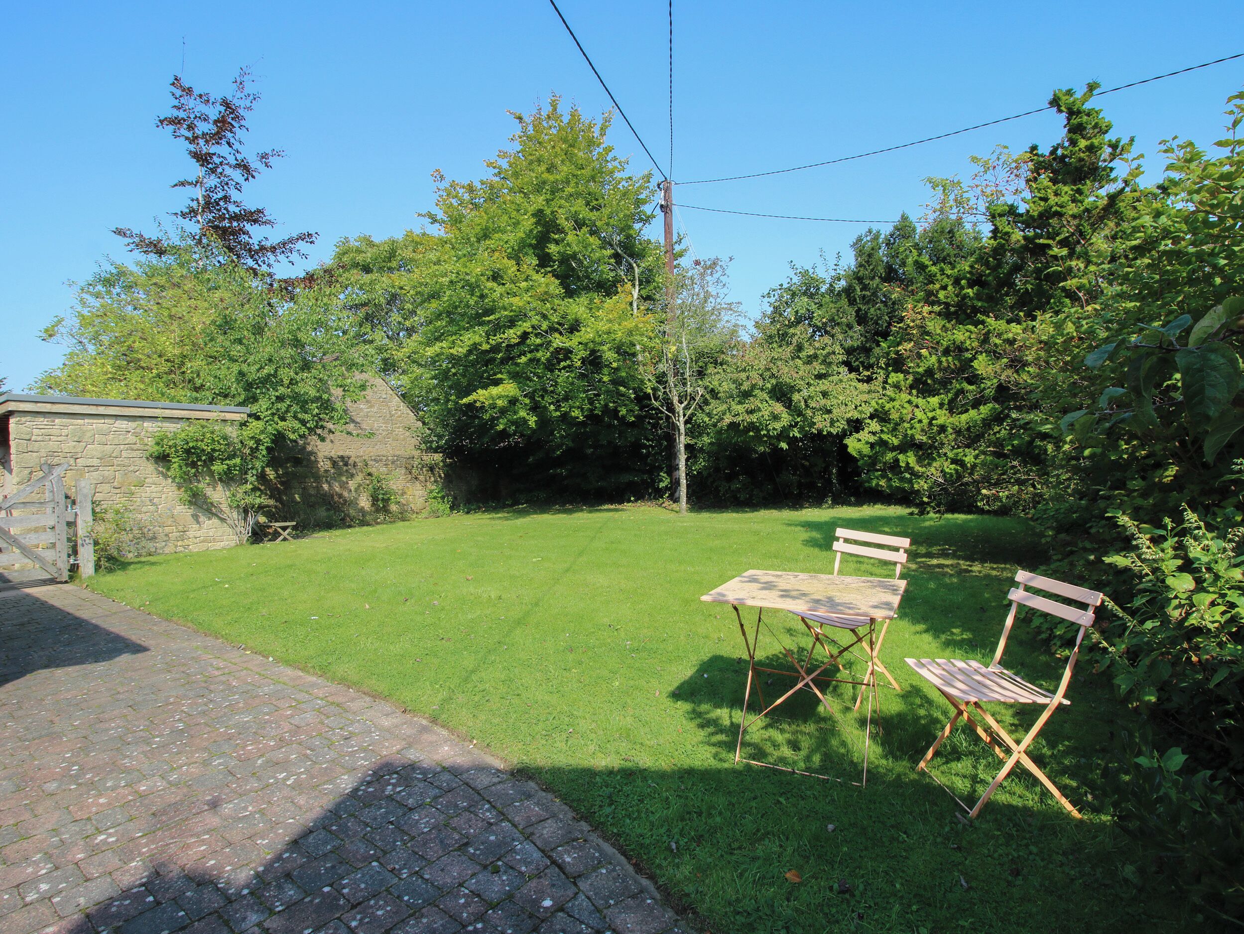 A grassy backyard with a stone wall, a wooden gate, and two folding chairs.