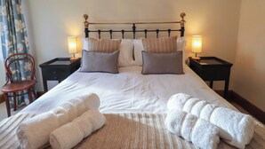 A neatly made bed with pillows and two bedside lamps, a chair, and a small table with a lamp. - Riverbank At Stepping Stones (Ambleside)