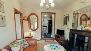 A living room with a brown leather sofa, a round coffee table, a fireplace, and a television. - Riverbank At Stepping Stones (Ambleside)
