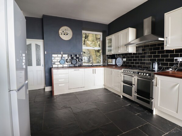 A modern kitchen with white cabinets, a black tiled backsplash, a large stove, and a window with a view of trees.