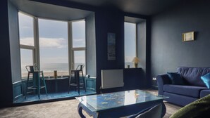A room with a view of the beach, a glass coffee table, a blue sofa, and two bar stools. - Tonnau Yr Oleu or Waves of Light (Barmouth)