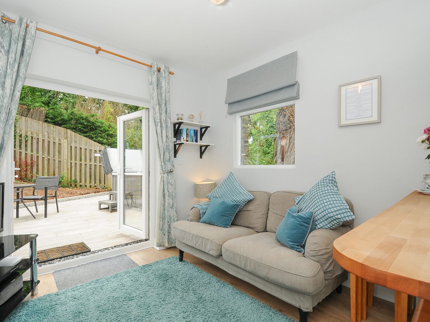 A cozy living room with a sofa, a dining table, and a view of a garden through a sliding glass door.
