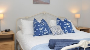 A neatly made bed with white and blue floral pillows, a blue towel, and a painting of a beach scene above it. - Tarka View (Bideford)