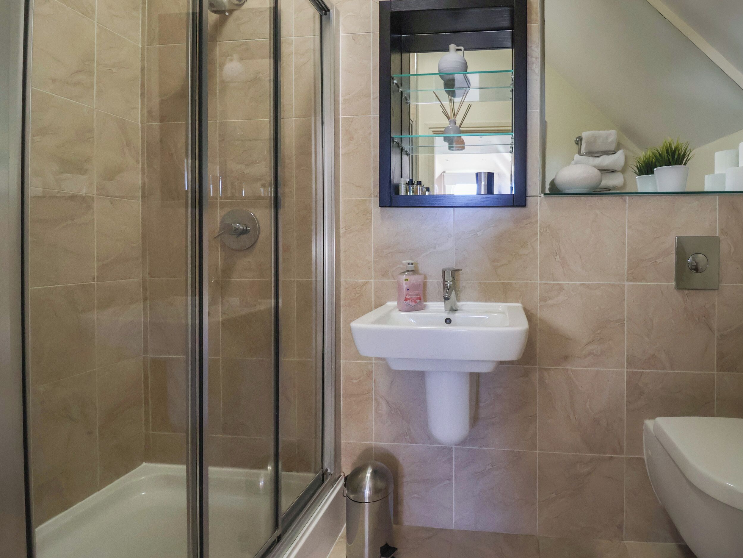 Une salle de bain avec une douche à parois de verre, un lavabo sur colonne et des toilettes.