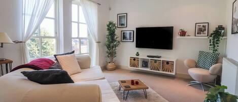 Ein Wohnzimmer mit einer Couch, einem Couchtisch, einem Fernseher und einer Pflanze.