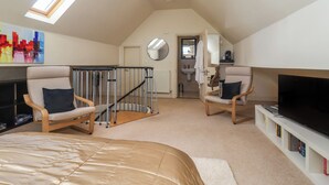 Une chambre spacieuse située dans les combles, avec un grand lit, deux fauteuils, une télévision et une lucarne.