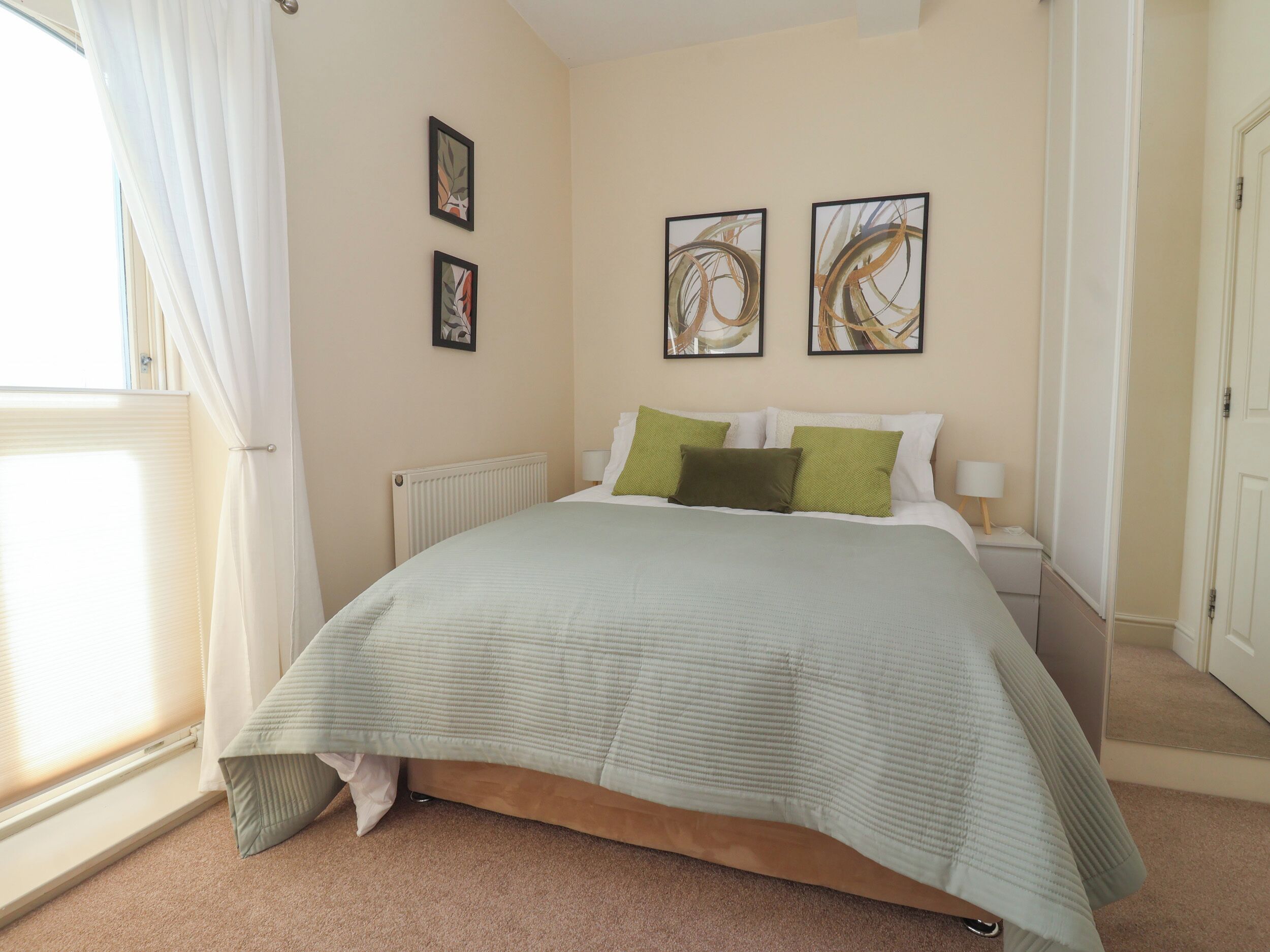 A bedroom with a bed, a radiator, and two framed pictures on the wall.