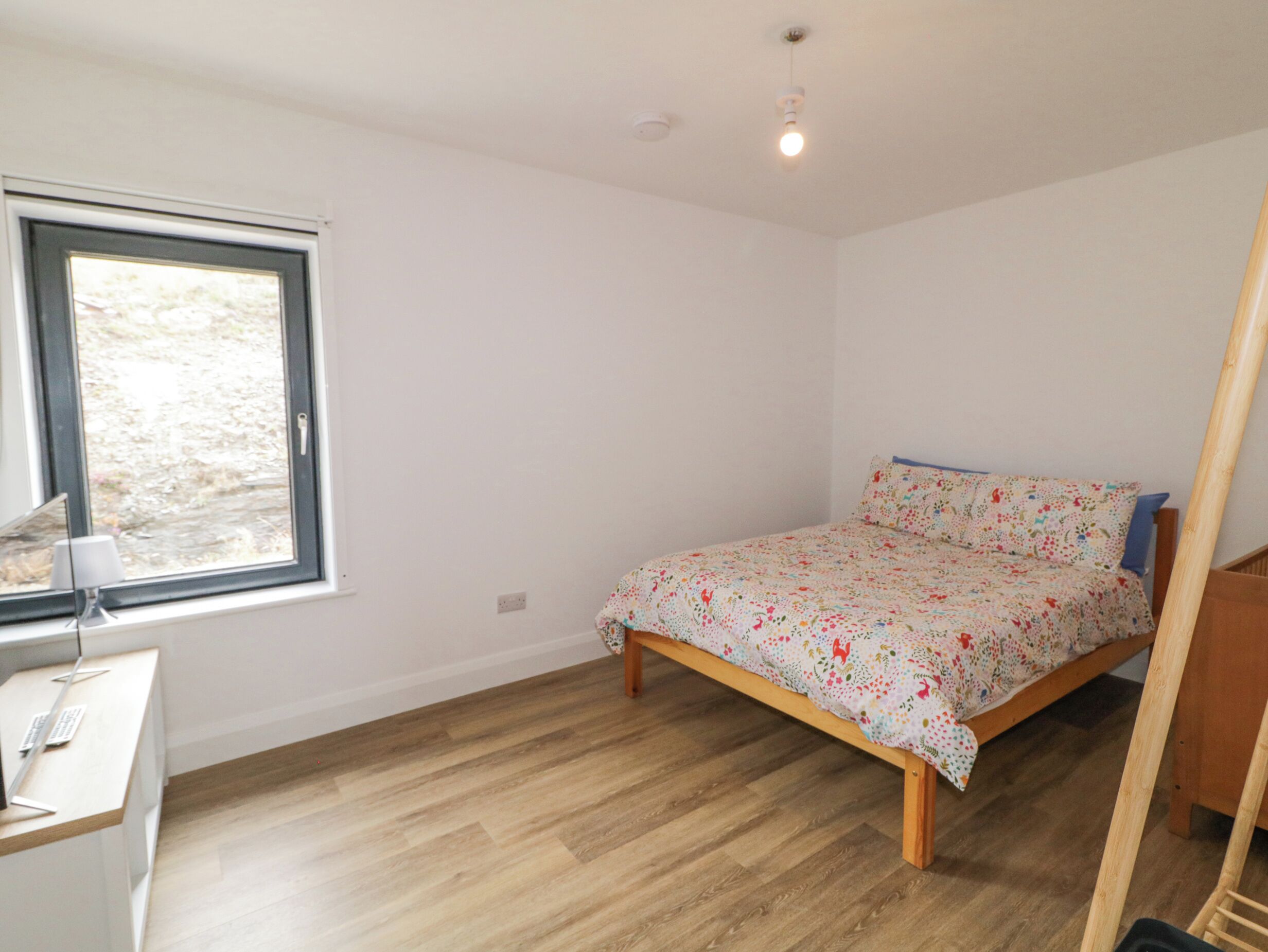 A bedroom with a wooden bed, a desk with a computer, and a window with a view of trees.