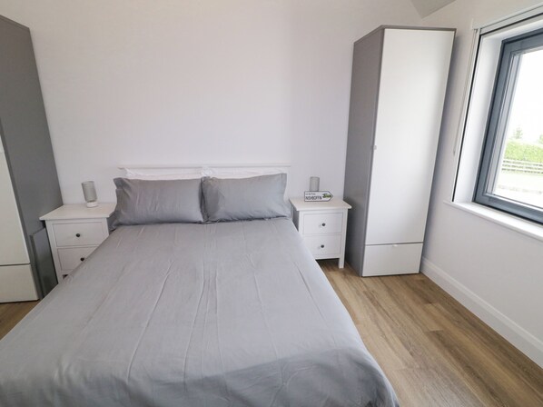 Un dormitorio con cama, mesitas de noche, armario y ventana.