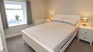 Une chambre bien rangée, avec un lit, des tables de chevet, une fenêtre avec des rideaux et un radiateur.