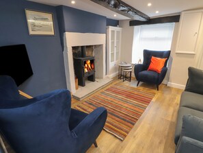 A cozy living room with a fireplace, blue armchairs, a striped rug, and a television. - Timekeeper's Cottage (Carnforth)