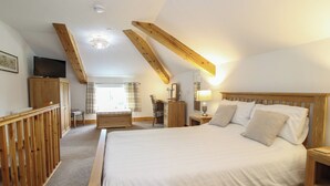 A bedroom with a large bed, wooden beams, a TV, a desk, and a window. - Ascot (Wrexham)