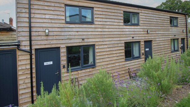 A two-story wooden building with multiple windows and doors, including a black door labeled "ASCOT". - Ascot (Wrexham)