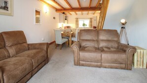 A cozy loft bedroom with exposed wooden beams, a dining area, and two brown leather sofas. - Ascot (Wrexham)