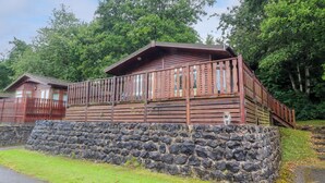 Eine rustikale Holzhütte mit Steinunterbau, einer Holzterrasse und einem Metallzaun.