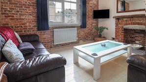 Un salon avec un mur en briques, un canapé en cuir, une table basse blanche, un téléviseur et une cheminée.