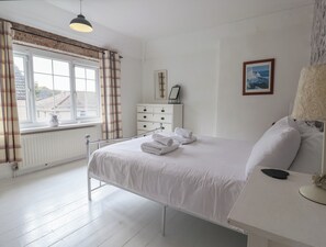 Une chambre à coucher avec un lit, une commode, une fenêtre avec des rideaux, un radiateur et un tableau accroché au mur.