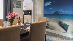 Un coin repas agrémenté d’une fresque représentant une plage tropicale, une cuisine en arrière-plan et un panneau d’accueil.