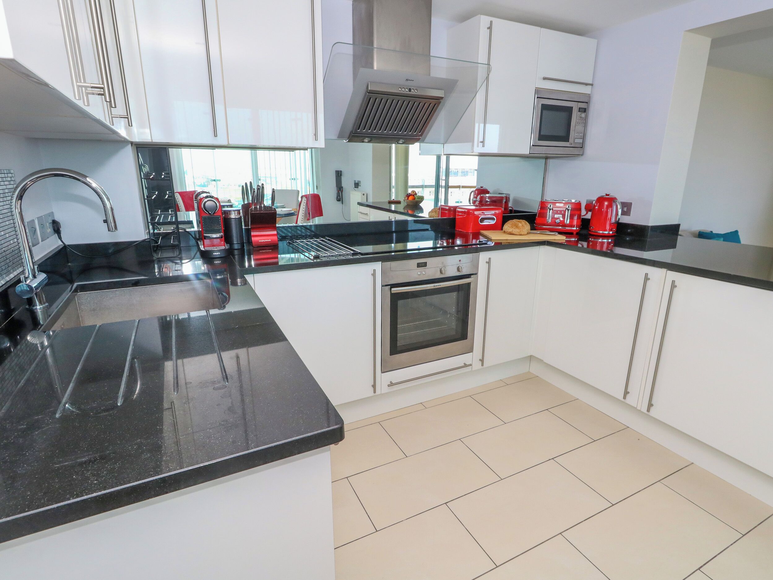 A modern kitchen with white cabinets, a black countertop, stainless steel appliances, and a red toaster.
