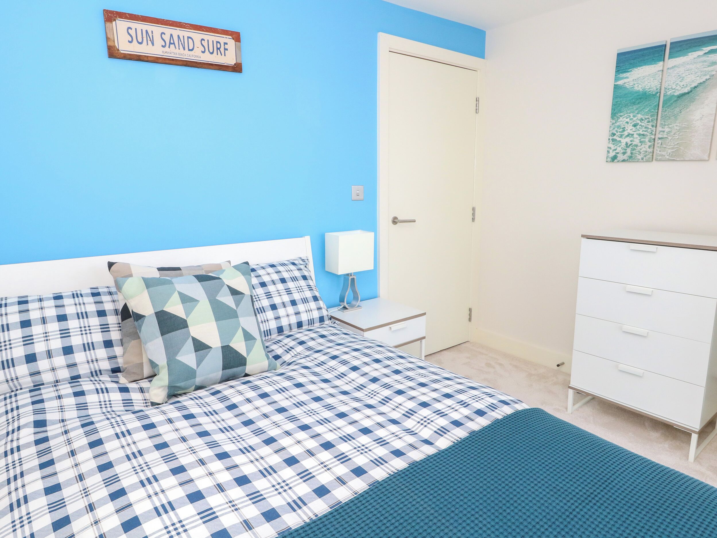 A bedroom with a bed, a nightstand, a dresser, and a wall sign.