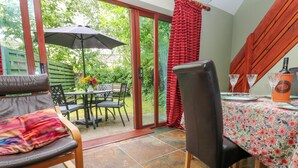 A dining area with a table set for four, a chair, a red rug, and a patio with a table and chairs under a canopy.