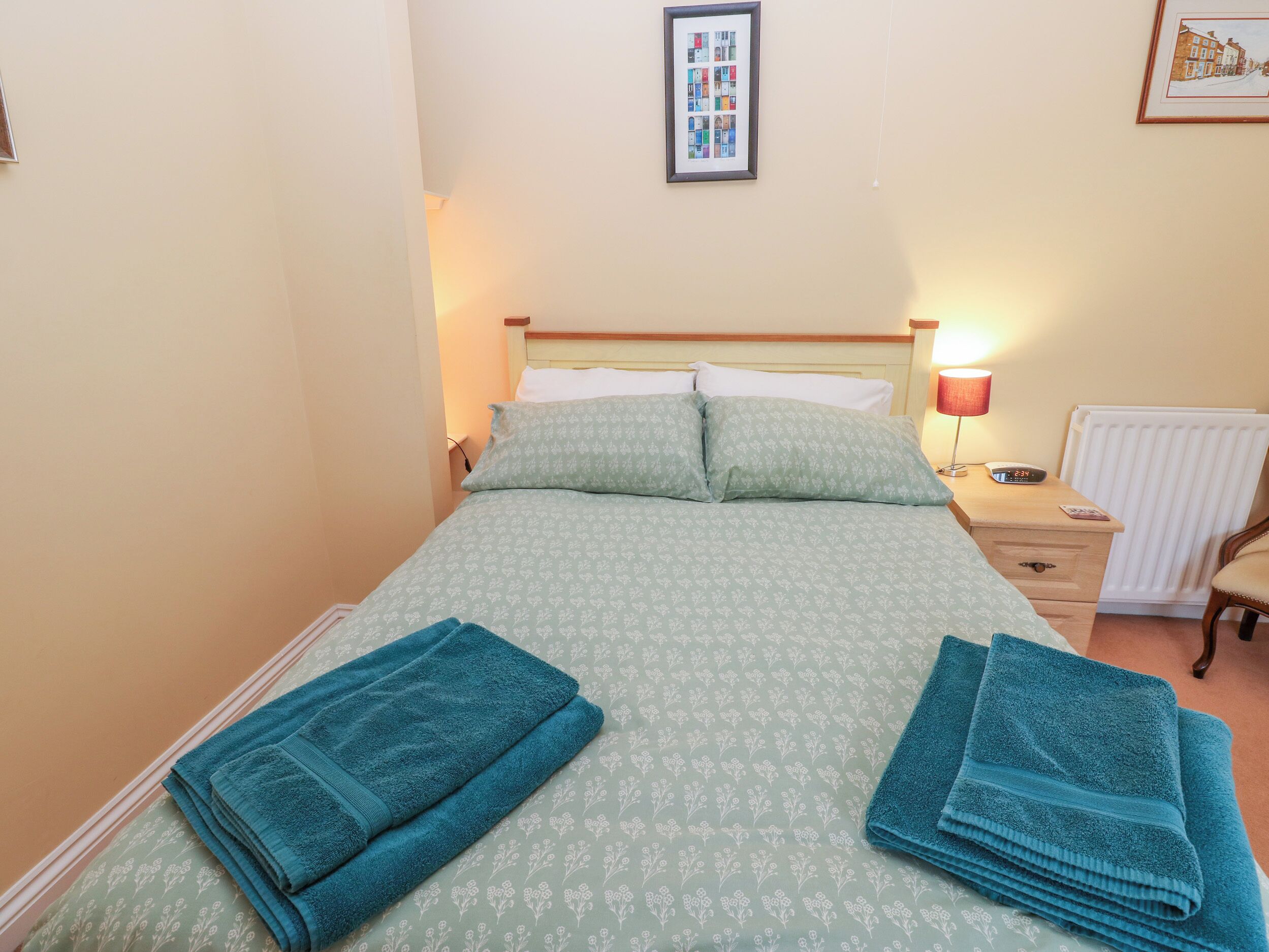A neatly made bed with a floral patterned bedspread, two pillows, and two folded towels on the side.