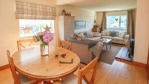 Een gezellige woonkamer met een eethoek, met een ronde houten tafel, stoelen, een bank en een salontafel.