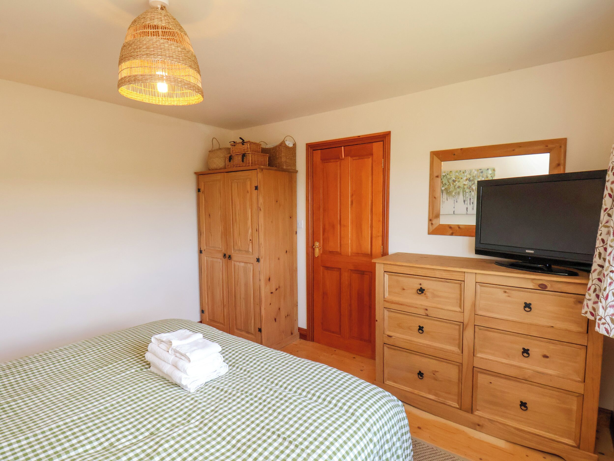 A bedroom with a bed, wooden wardrobe, dresser, television, and a hanging light fixture.