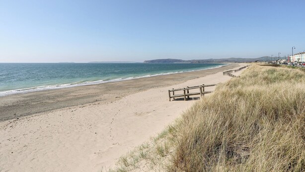 A beach with a wooden walkway, sandy dunes, and a clear view of the ocean and distant hills. - Harbourside Apartment (Pwllheli)