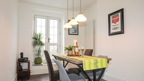 A dining area with a table set for two, a potted plant, a candle, and a framed picture on the wall. - Harbourside Apartment (Pwllheli)