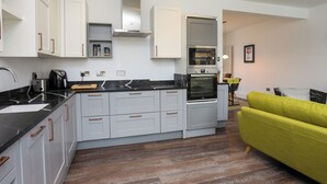 A modern kitchen with integrated appliances, grey cabinetry, and a wooden floor. - Harbourside Apartment (Pwllheli)