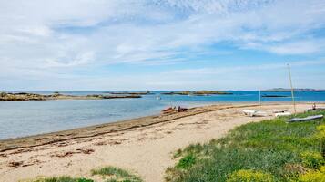 A beach with boats, a tractor, and a lighthouse in the distance.