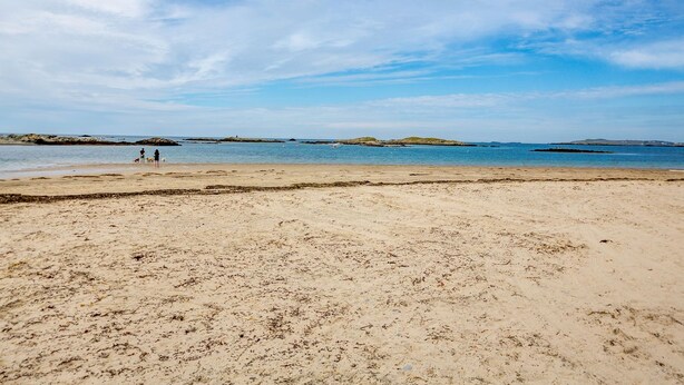Une plage de sable fin, avec un ciel dégagé et une mer calme.