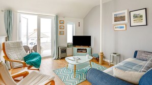 Un salon chaleureux avec un canapé, un fauteuil et un téléviseur. Il y a une fenêtre avec des rideaux, une petite table avec une tasse et un tapis à motifs.