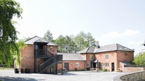 A brick building with a staircase leading to an upper level, a gravel driveway, and a stone fire pit. - Woodside Cottage (Newtown)