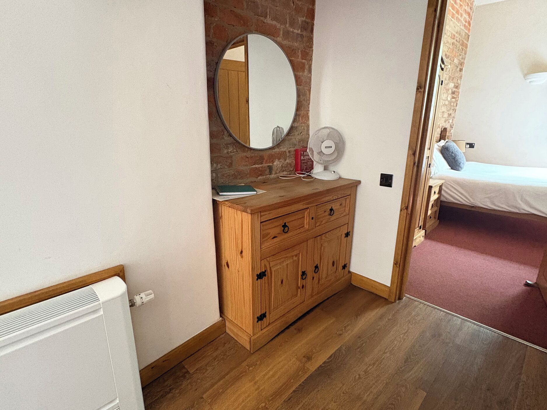 A bedroom with a wooden dresser, a mirror, a fan, and a bed with a pink carpet.