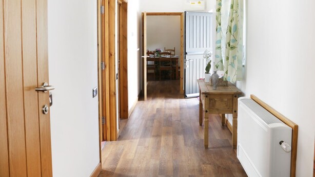 A hallway with wooden doors, a radiator, and a dining area in the background. - Woodside Cottage (Newtown)